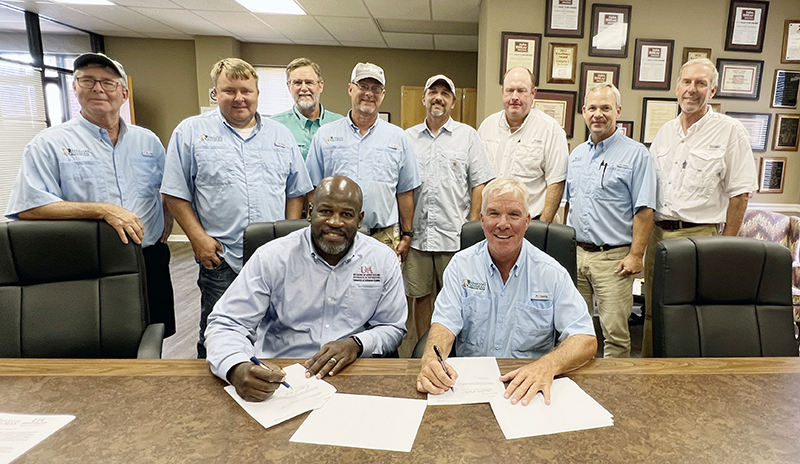 Members of the Ark Soybean Promotion Board stand behind head of division of ag and board chairman as they sign an agreement at table.