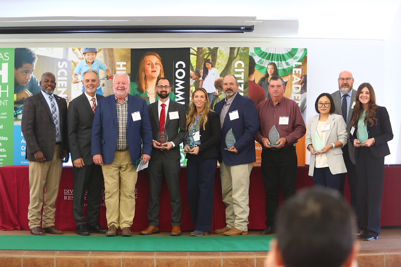 A group of people gathered around a green tractor in a rural setting, discussing its features and operation.