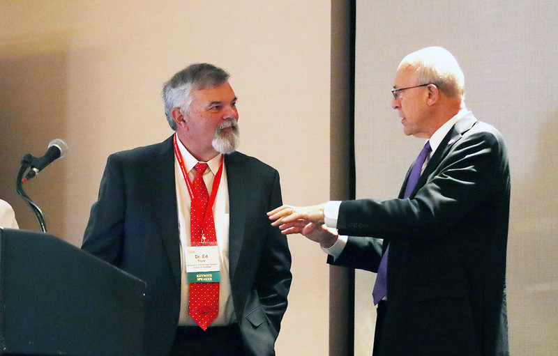 Keynoter Ed Fryar on left, speaks with Division of Ag interim VP Chuck Culver, right on the dais before Fryar speaks.