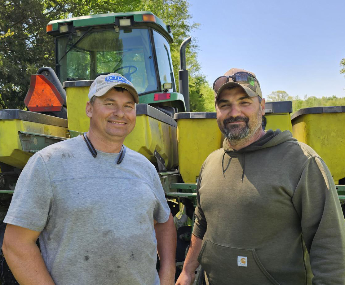 Two men standing in front of a tractor.