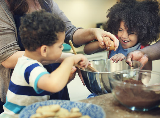 mom assisting daughter with cracking an egg while her brother mixing the ingredients