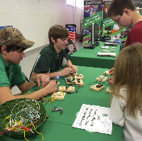 Older youth at a table showing kids how to build a circuit