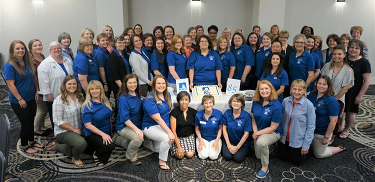 Group of NEAFCS members wearing blue logo shirts standing in a group smiling. About 40 women total.