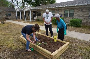 one woman bending over gardening and two people standing nearby