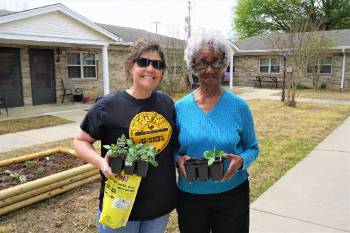 Two women holding plants in front of building