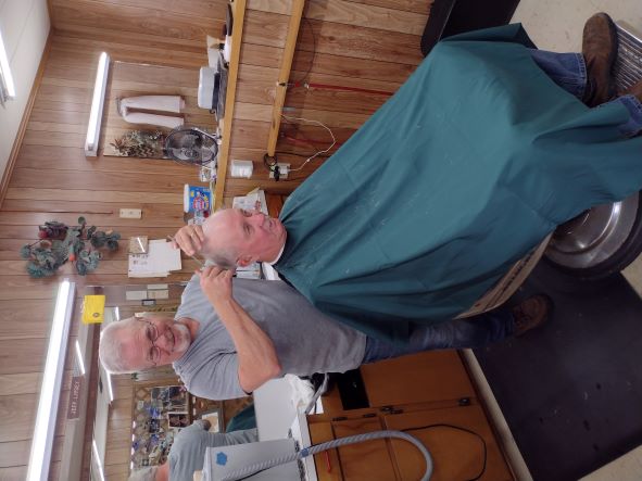 Man cutting seated man's hair while looking at camera