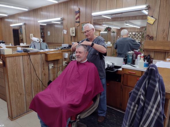 man standing behind a seated man, cutting his hair 