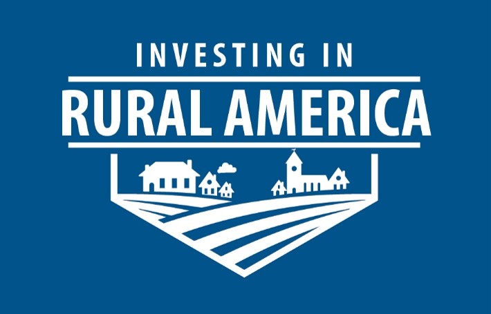 logo of the Federal Reserve Bank of Richmond’s Investing in Rural America program. It is titled “INVESTING IN RURAL AMERICA” and is stylized with a rural landscape with farm fields, houses, and a church on a blue background.