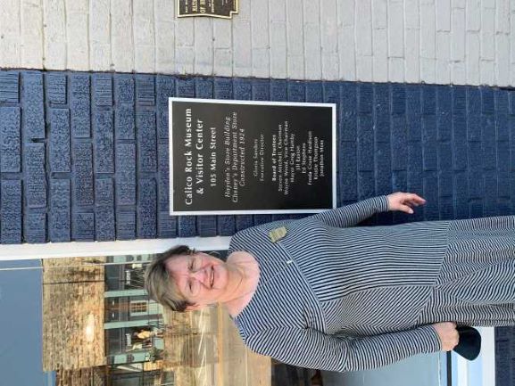 Women in black and white striped dress stands in front of blue building with sign for museum