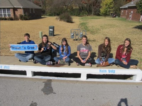 4-H youth sitting on top of a recently painted storm drain
