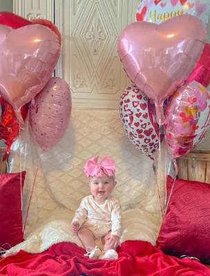 Baby sitting in front of six heart shaped balloons