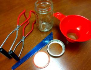 canning supplies on a table including tongs, jars and lids, and a funnel