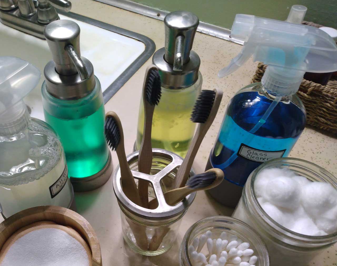 overhead view of toothbrushes in a holder alongside several unlabeled reusable bottles of cleaner