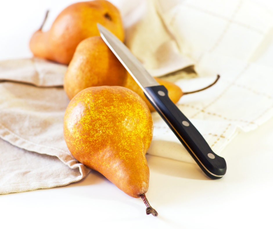 Three bosc pears on a table with a knife balanced on top of the one in the foreground