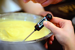 hand holding a candy thermometer dipped into a pot of melted white chocolate