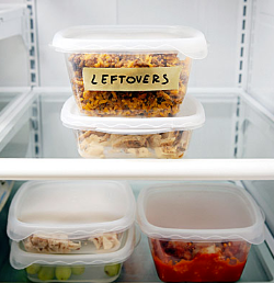 Stacked plastic containers with leftover food on two shelves inside refrigerator