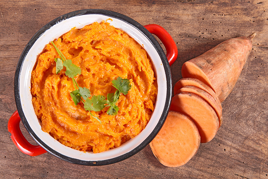 bowl of mashed sweet potatoes seen from above with a sliced sweet potato next to it