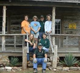 Old house with seven men and women sitting and standing on the front steps