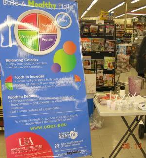 Picture of a poster displaying the myPlate logo, there is also nutritious snacks in the back ground at a local grocery store.