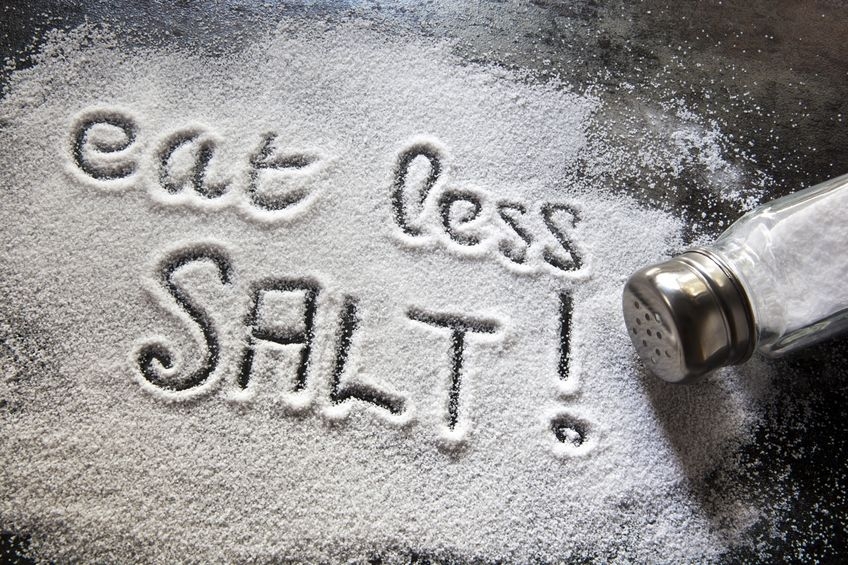 Eat Less Salt written in salt from an empty salt shaker nearby