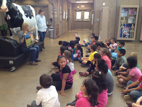 youth gather around large dairy cow at Ag Learning Center, Four States Fairground, to learn about various farms available in Arkansas