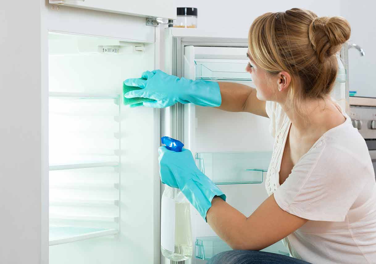 woman with gloves on spraying the inside of refrigerator