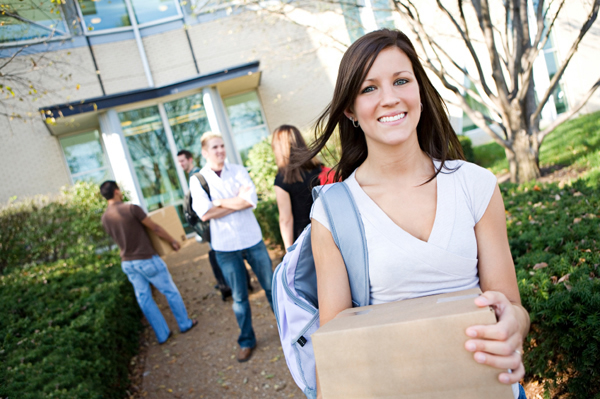 college students walking towards the dorm with a care package in her hands with other students in the background.