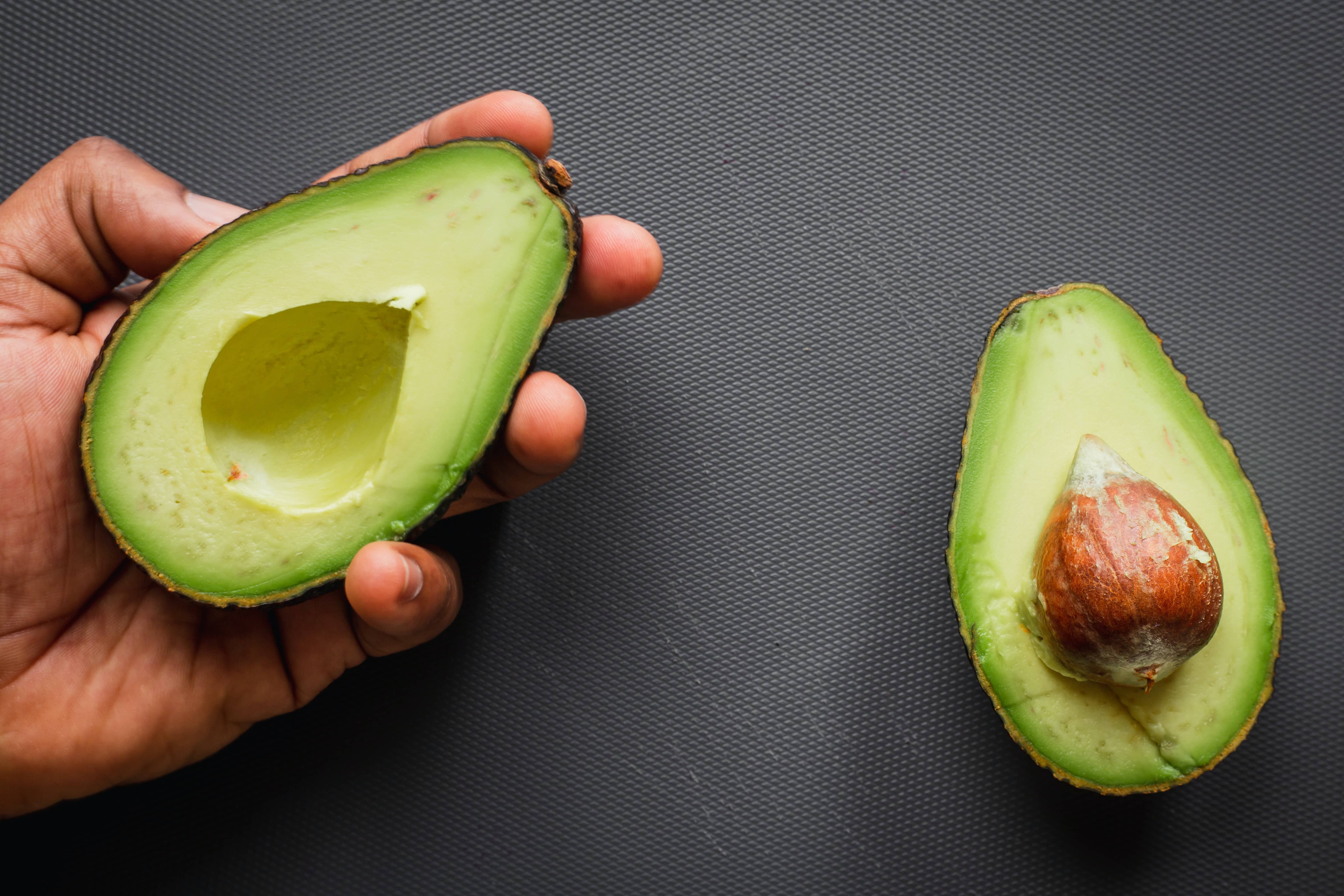 avocado sliced in half with large seed inside one half, along with a dish made with avocado.