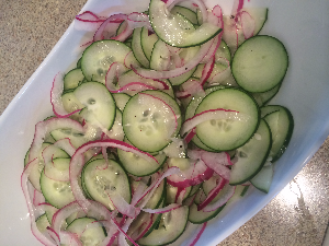 sliced cucumbers and onions on platter with vinegar, sucrolose, salt and pepper