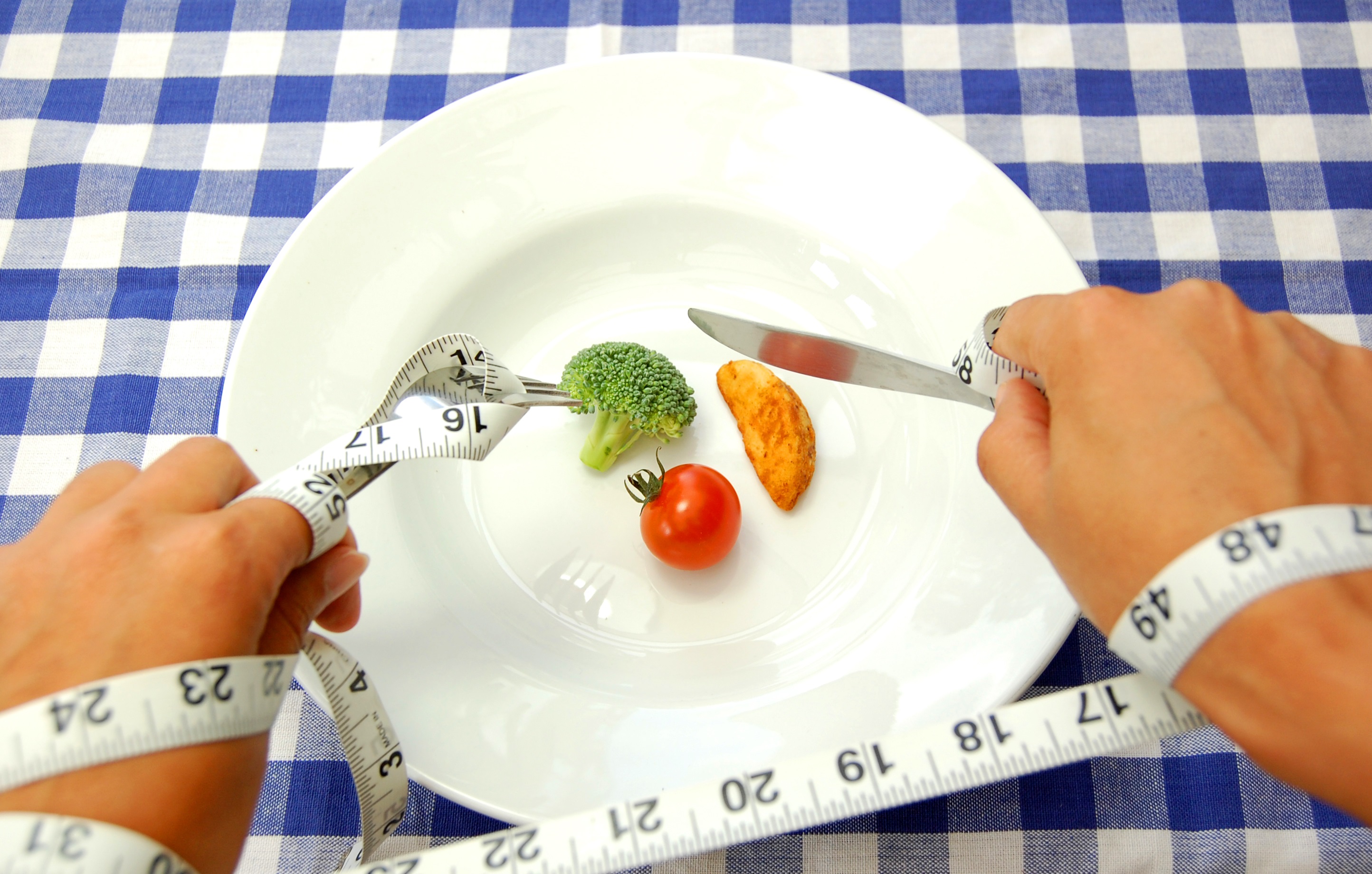 tape measure around person's arm, restricting movement. In the plate is a tiny amount of little broccoli and tomato
