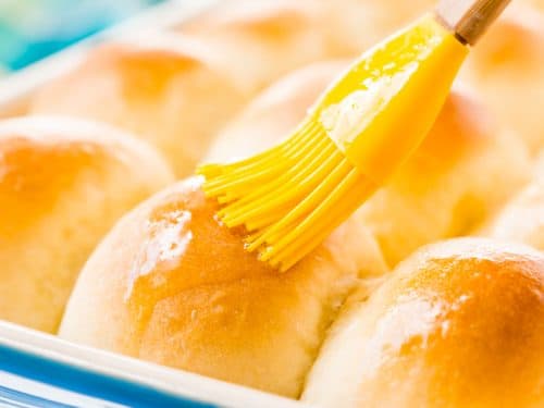 homemade yeast rolls in pan with melted butter being spread over them