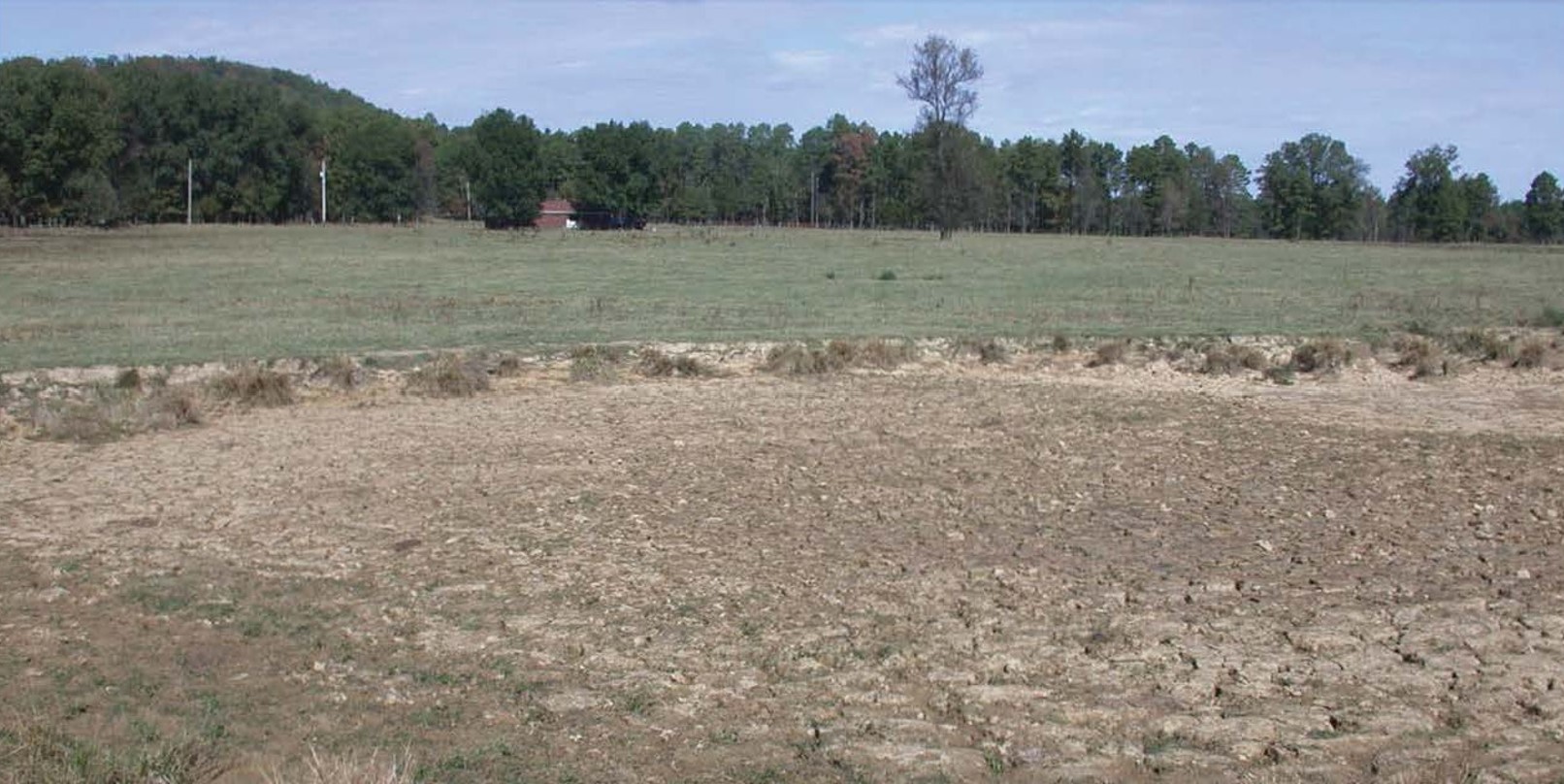 Effects of drought in Arkansas, with a dried pond in the foreground and a pasture with minimal forage in the background.