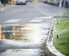 sprinkler on a lawn creating water pooling in the street