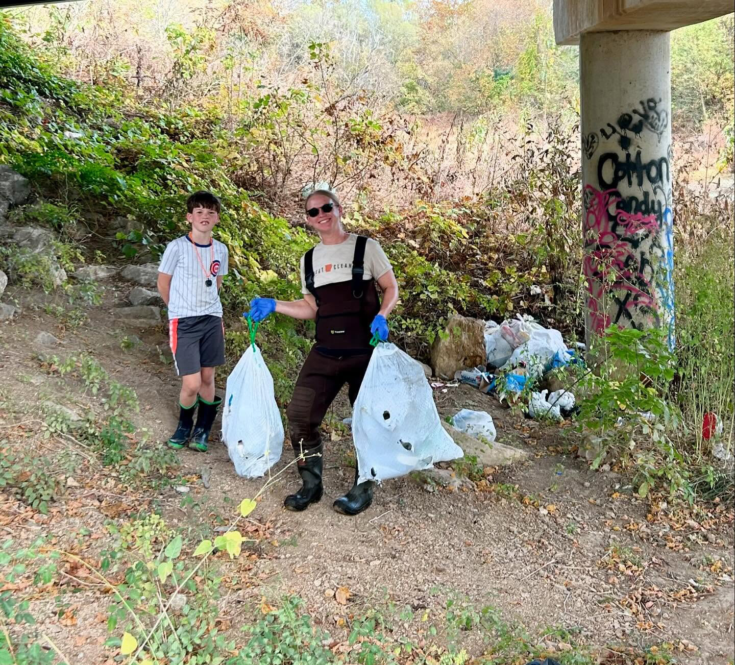 A woman and boy clean up trash in a creek