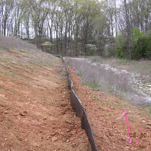 silt fence that is black plastic material with the bottom of the fence flush with the dirt to keep it from eroding