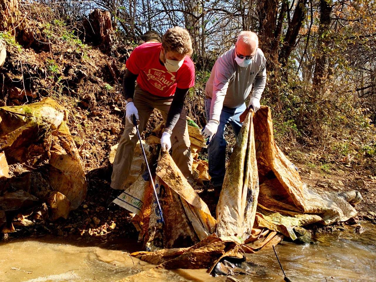 Two volunteers removing trash from creek