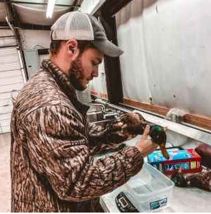 Young man in cap and camoflague looking at a dead mallard in a laboratory