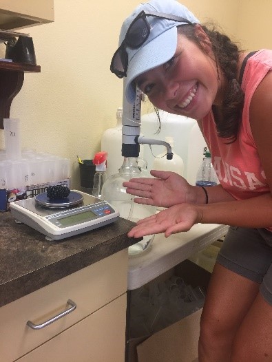 Photo of young girl posing next to a large blackberry sitting on a scale in a laboratory