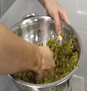 Grapes being pressed through a metal colander by hand