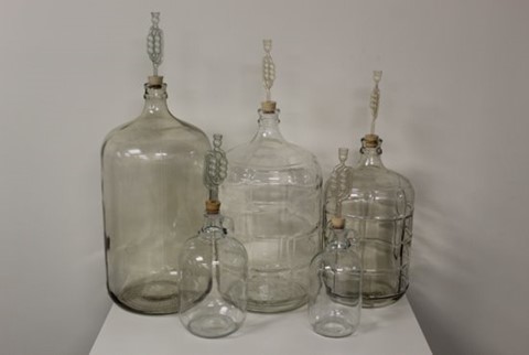 A set of glass jugs of various sizes with fermentation locks on the tops used for winemaking
