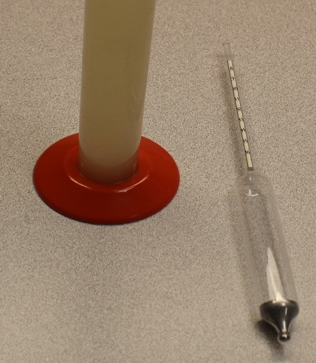 A hydrometer laying next to a graduated cylinder of grape juice