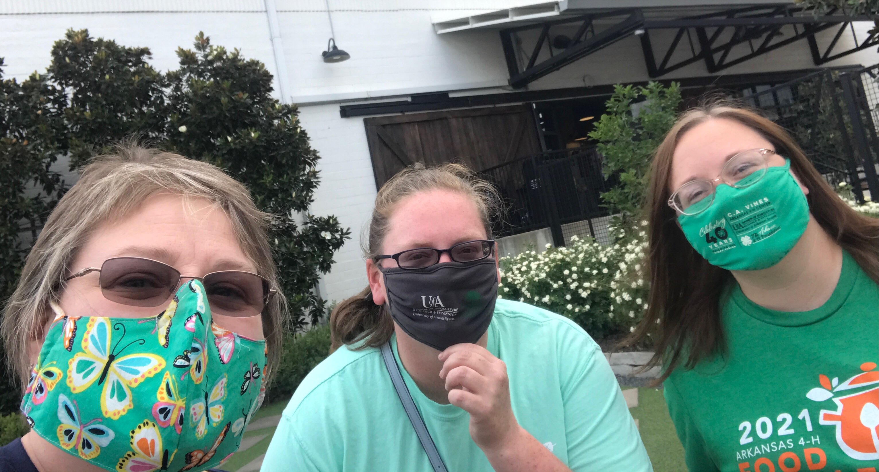 Three women posing together while wearing masks