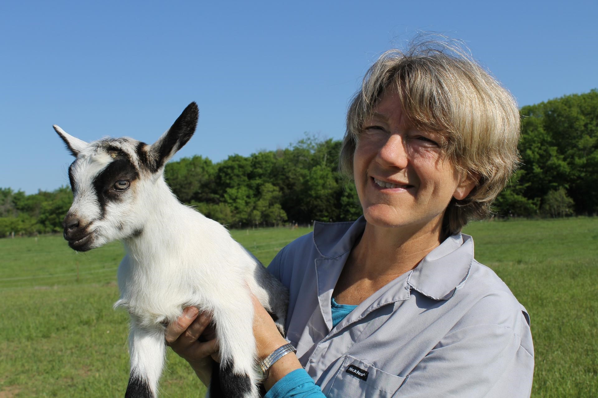Linda Coffey in an open field holding a baby goat