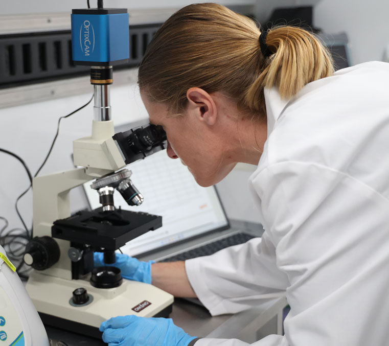 Woman in lab coat, looking through a microscope