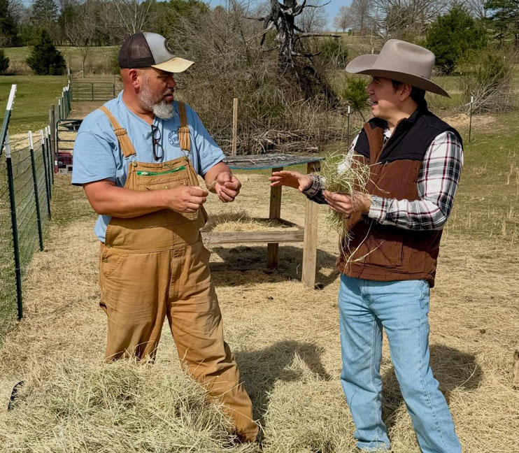Two men talking over a bale of hay