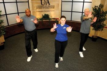 One woman and two men in a row doing balance exercises with arms outstretched in front of them and right foot slightly forward.