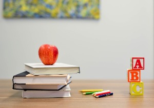 Picture of desk with an apple on a stack of books, colored pencils, and "A, B, C" blocks