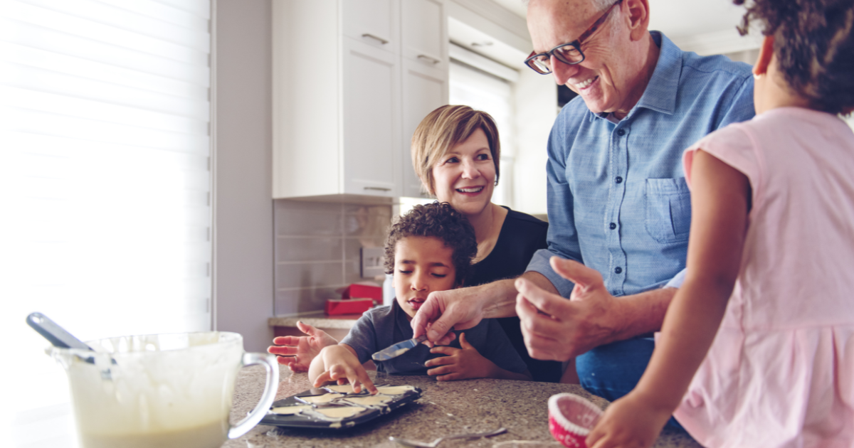 grandma and grandpa in a kitchen cooking pancakes with two young children at the counter