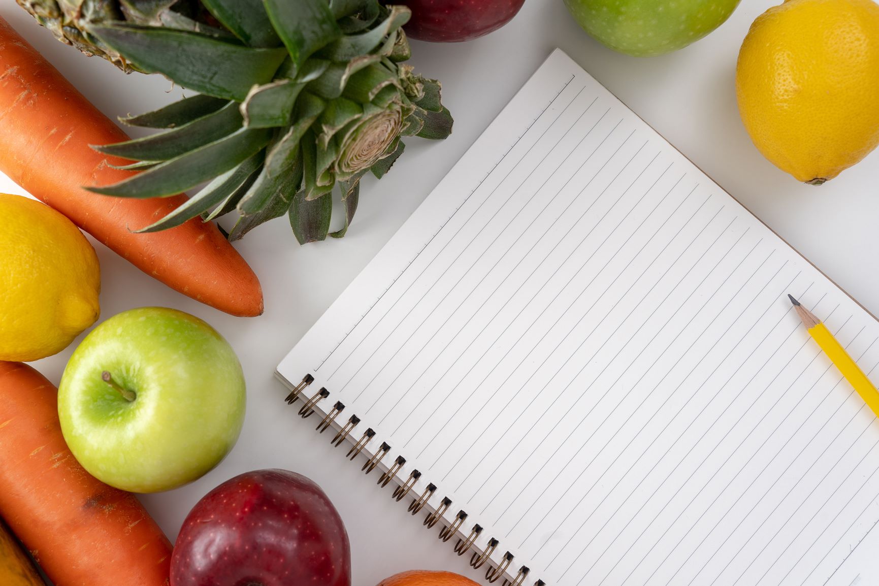 spiral notebook and pen surrounded by fruits and vegetables