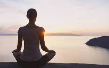 woman facing away from camera sittng on the beach meditating